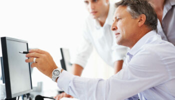 Mature business man discussing project with his colleagues and pointing at computer screen